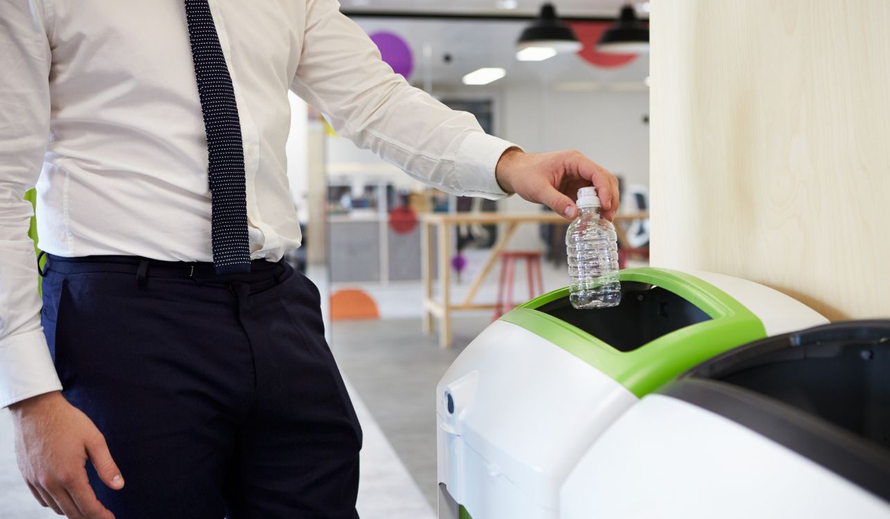 Man putting plastic bottle in recycling bin at an office.